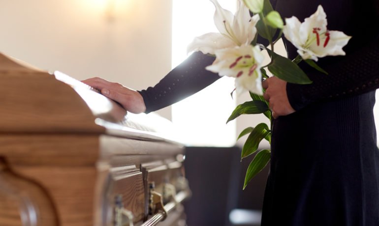 woman with lily flowers and coffin at funeral