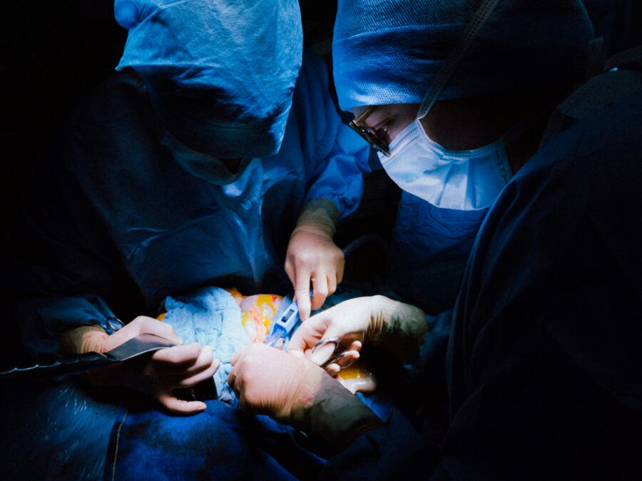 Surgeons in a dimly lit operating room performing a surgical procedure, illuminated by bright, focused lights, wearing blue surgical gowns, masks, and gloves.